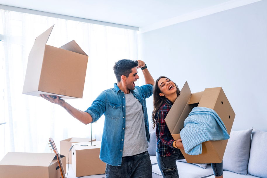 A happy couple unpacking cardboard boxes in their new home at the end of the moving process.