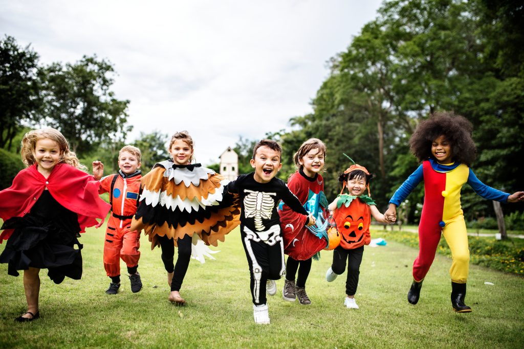 A group of young kids running across the grass in their Halloween costumes.