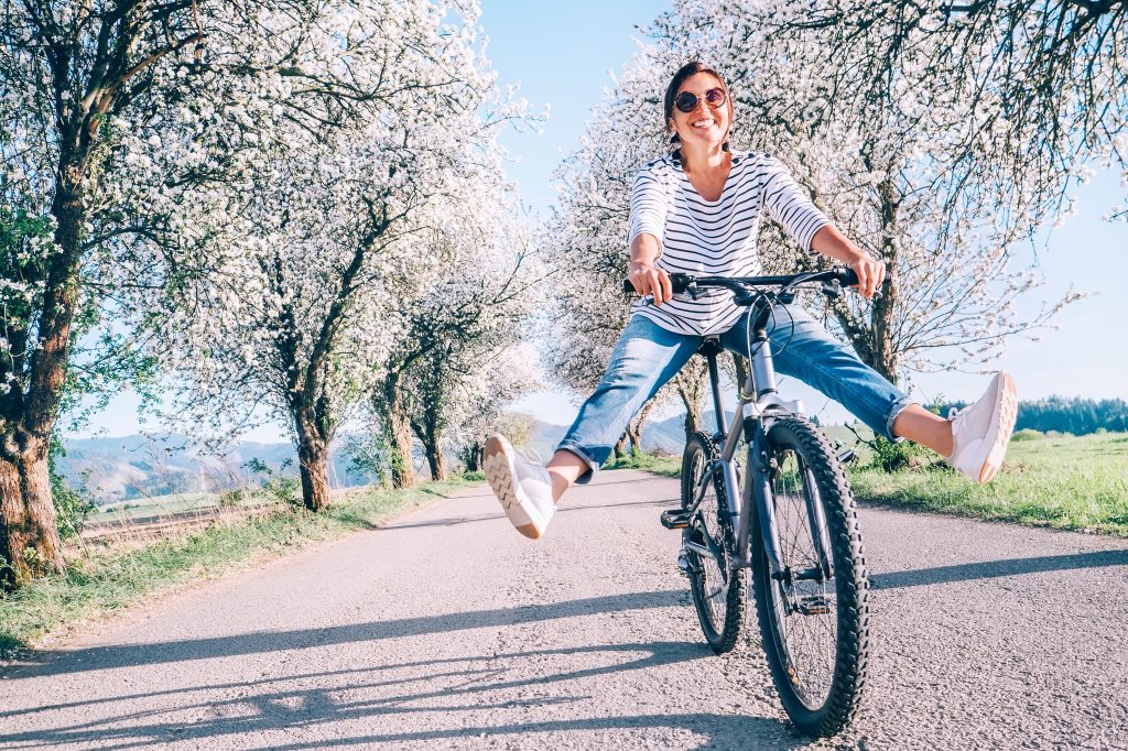 Woman riding a bicycle on a street lined with blossoming trees.