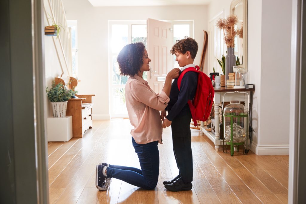 A mom kneeling in front of her young son in the foyer, getting him ready for school.