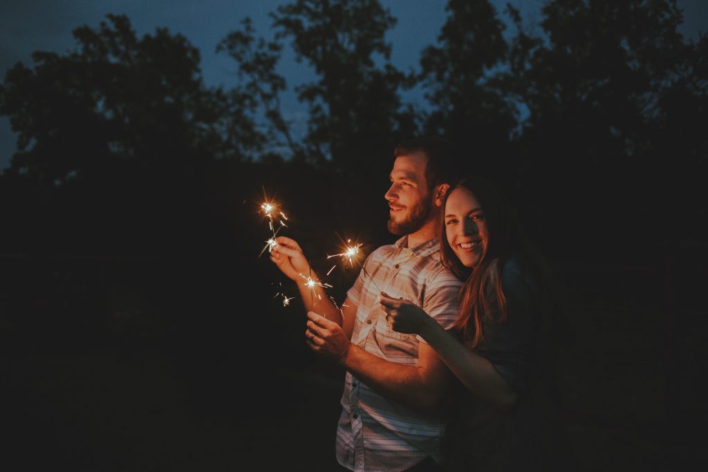 A couple smiling and holding sparklers in the dark.