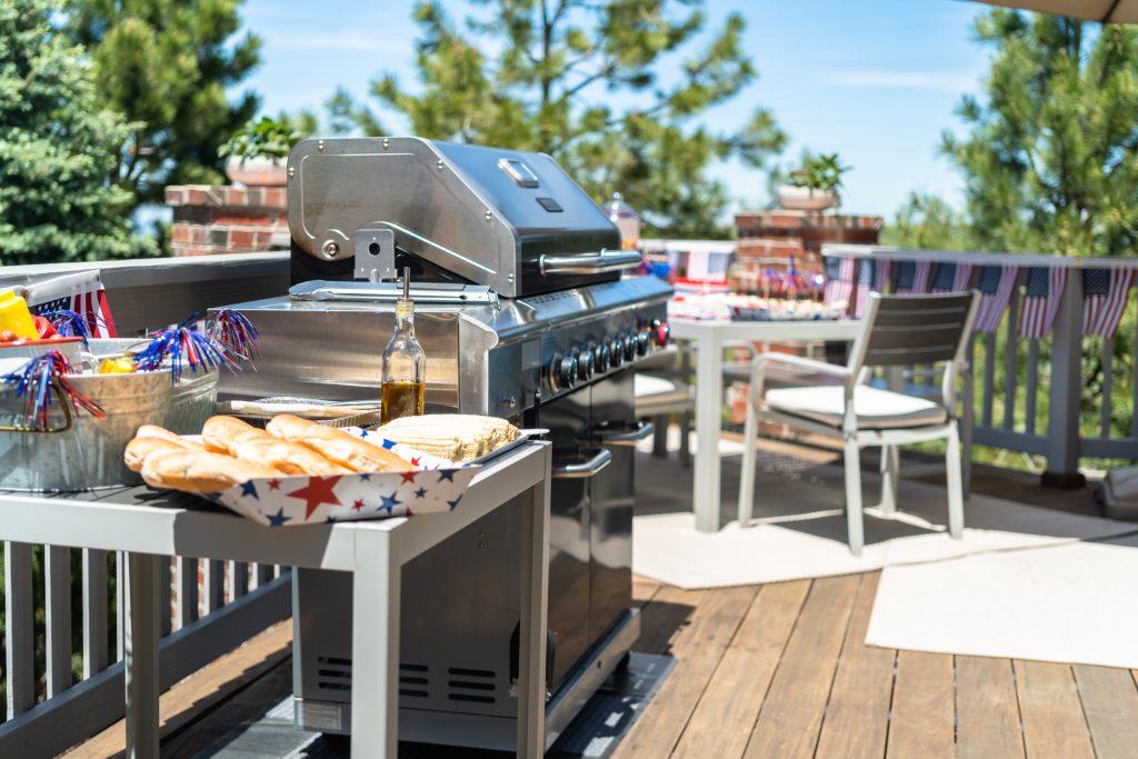 A patio with a grill and hotdogs on patriotic-themed plates.