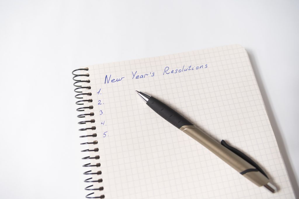 A notebook and pen with the text "New Year's Resolutions" and a blank numbered list.