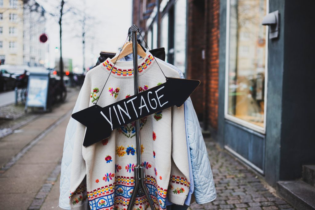An outdoor rack of clothes with a sign pointing toward the storefront that says "vintage."