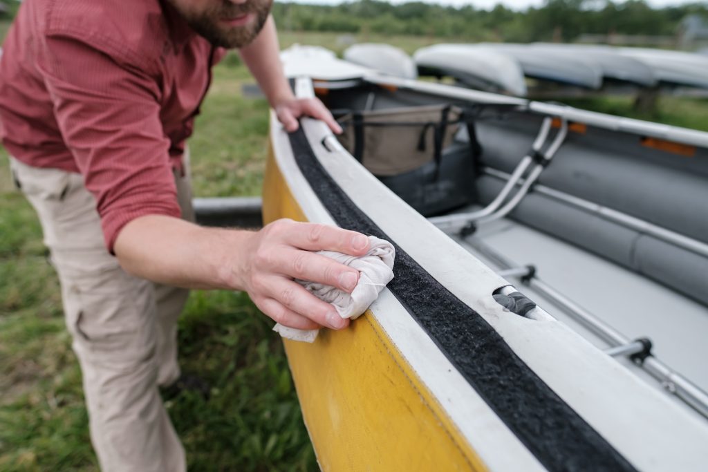 A man wiping dry the side of a canoe with a rag.