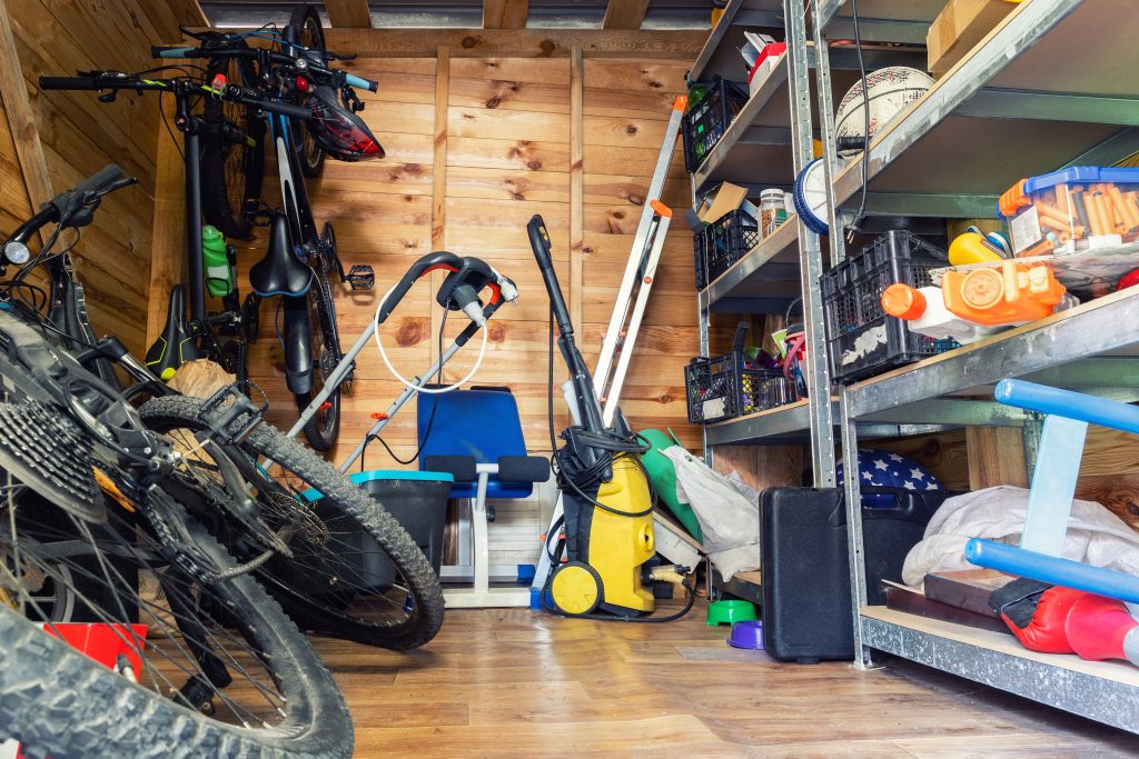 A disorganized outdoor shed with bikes, tools, and lawncare equipment.