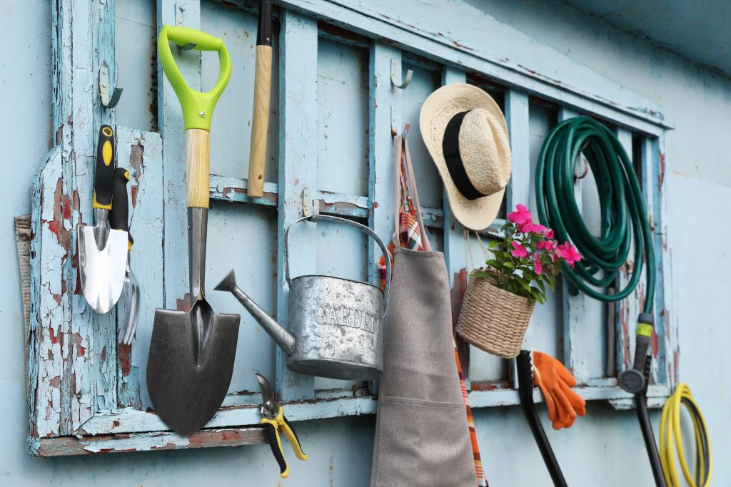 Gardening tools hanging on a wooden frame on the wall of a shed.