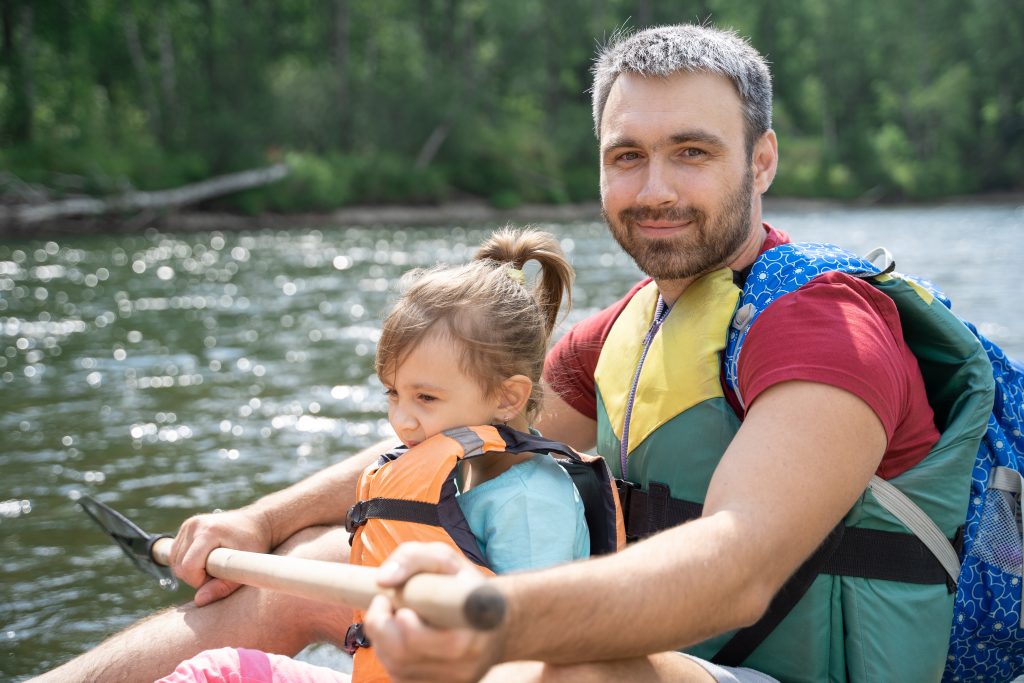 A dad and daughter on a kayak wearing life jackets.
