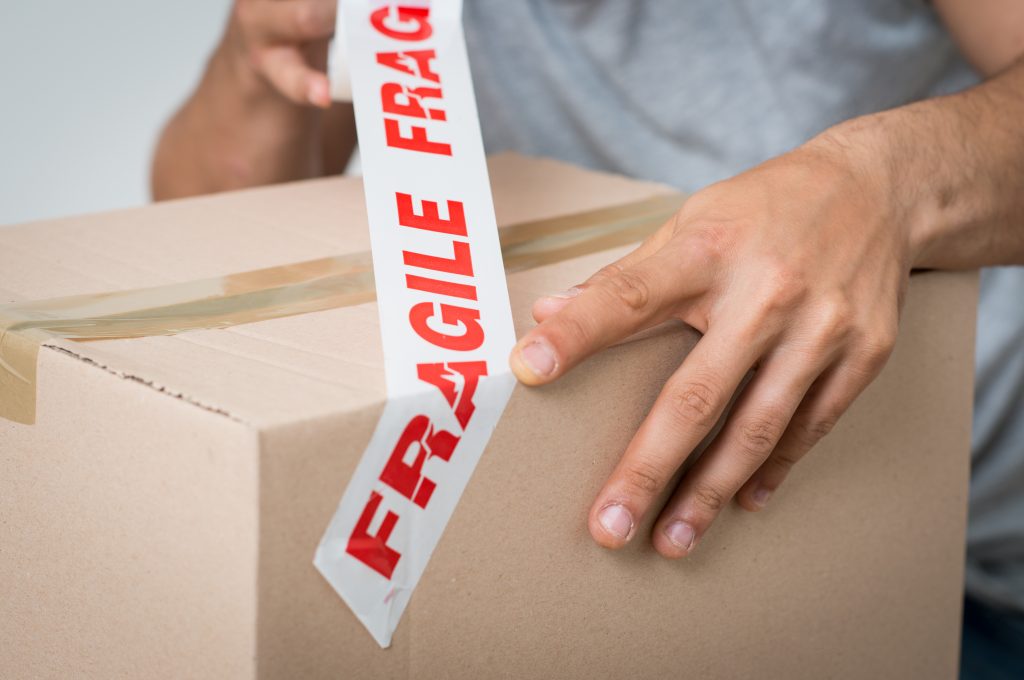 A man taping a cardboard box with tape that says "fragile".