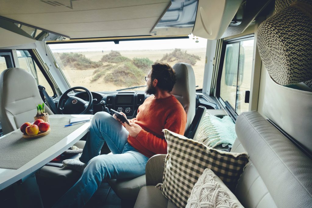 A man inside of an RV Camper looking out the windshield at sand dunes.