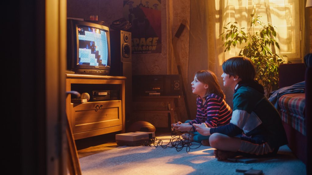 Two young kids playing a vintage video game on a box TV in a living room.