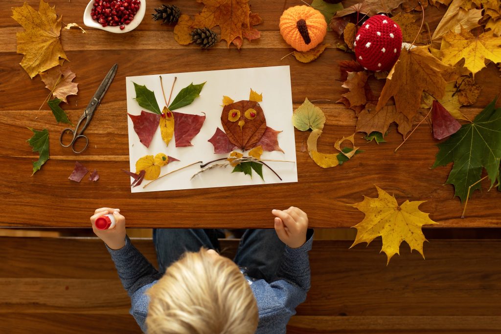 A toddler doing crafts at a table with fall leaves.