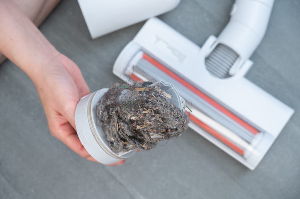 A hand holding a dirty vacuum filter next to a vacuum.