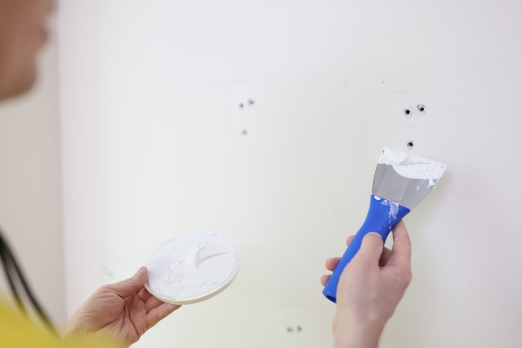 A person using spackle and spackle knife to repair holes in a wall.