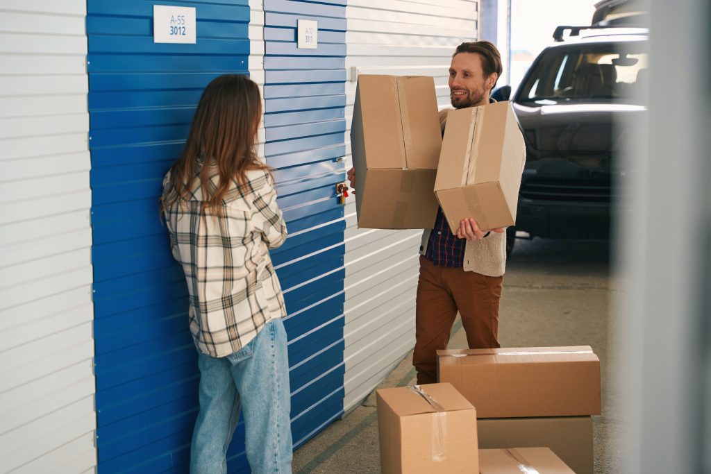 A man and woman unloading boxes from a car next to a self storage unit.
