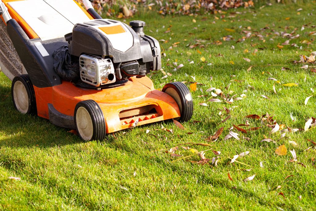 A lawnmower being pushed across a green lawn scattered with leaves.