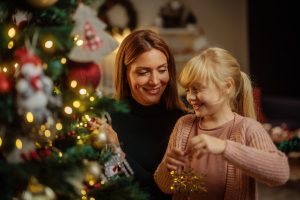 Woman and her young daughter putting ornaments on a Christmas tree.