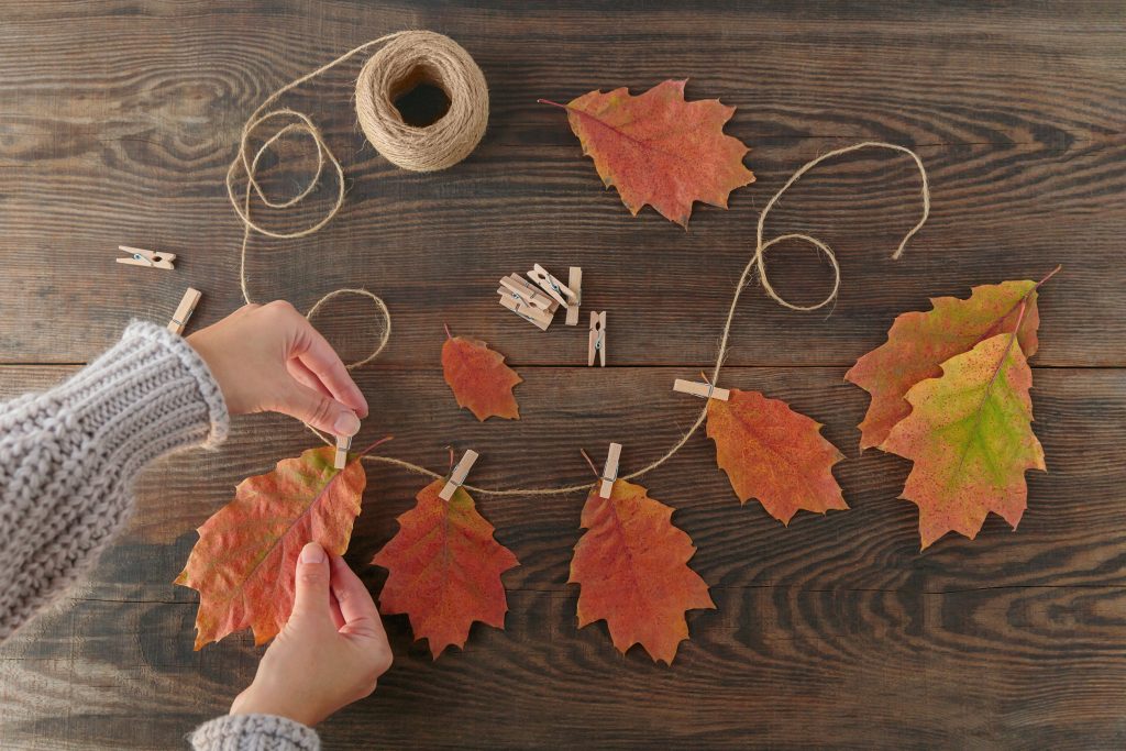 Hands pinning leaves to a strand of twine with clothespins.