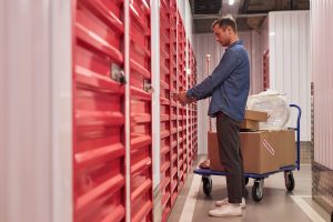 Man unlocking a self-storage unit with boxes near his feet.