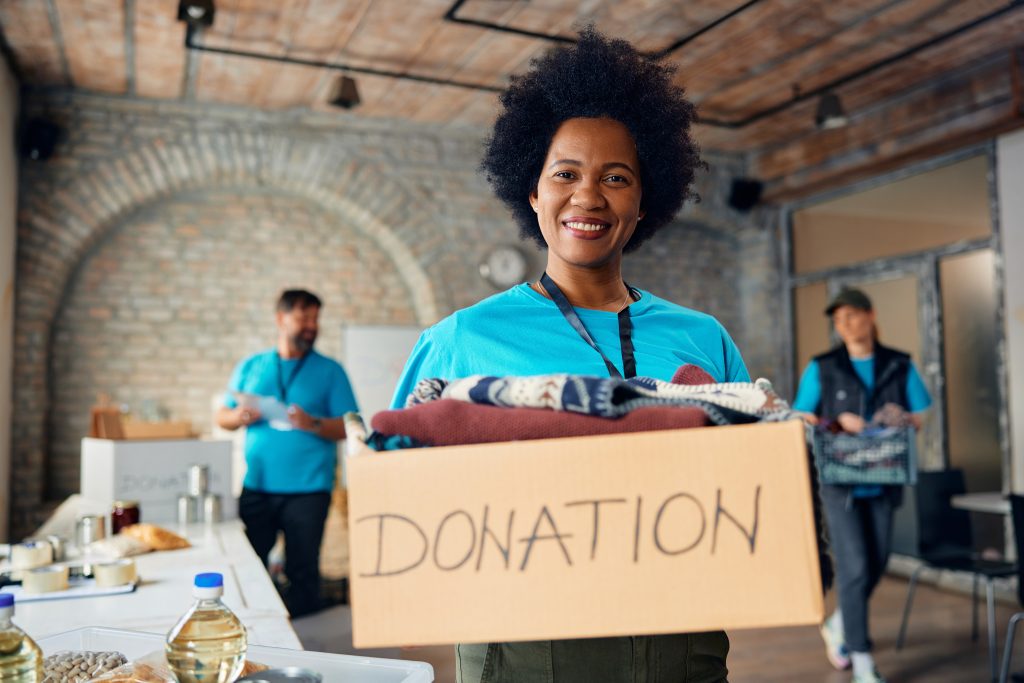 A volunteers holds a box labeled "Donation" while smiling.
