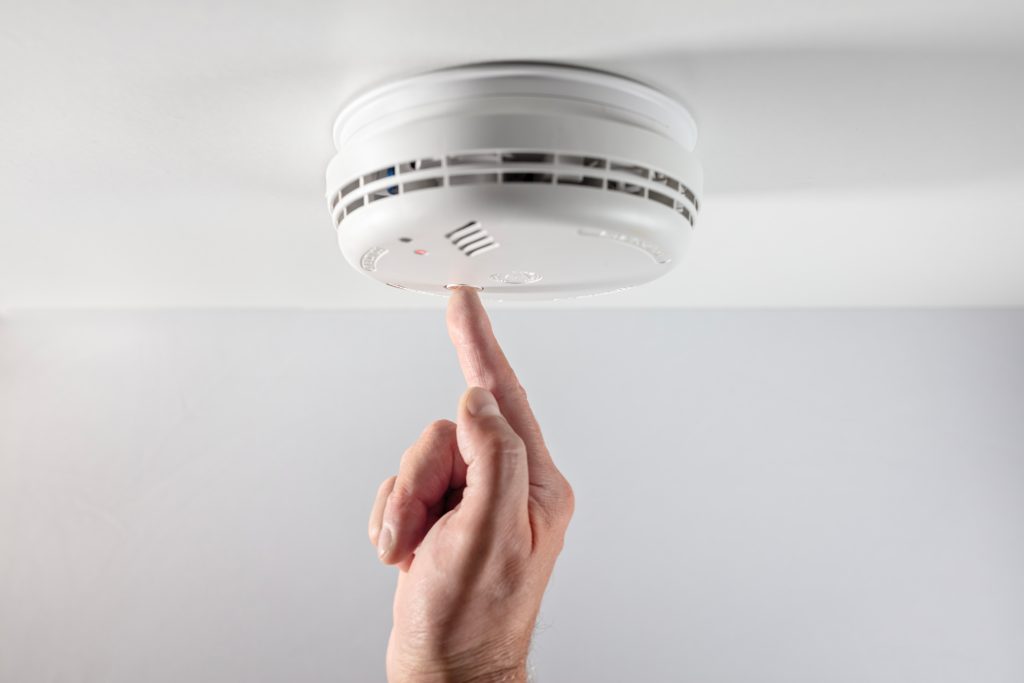 A hand reaching up to test a smoke detector.