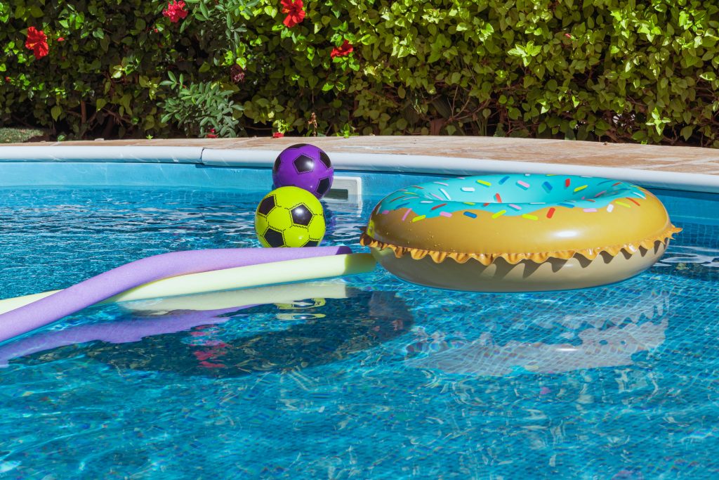 A pool with an inner tube, pool noodles, and floating balls on the surface.