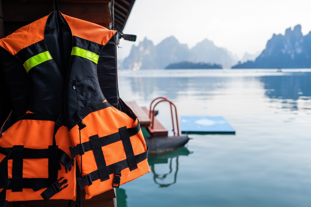An orange and black life jacket hung up to dry on the side of a shed near a lake.