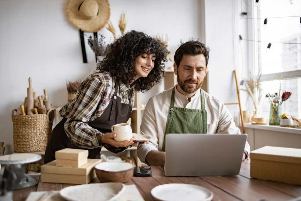 A man and woman in a pottery store looking at a laptop.