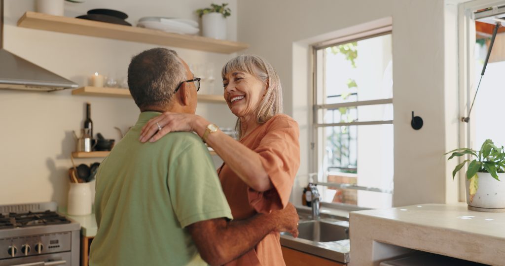 Senior couple dancing happily in a kitchen.