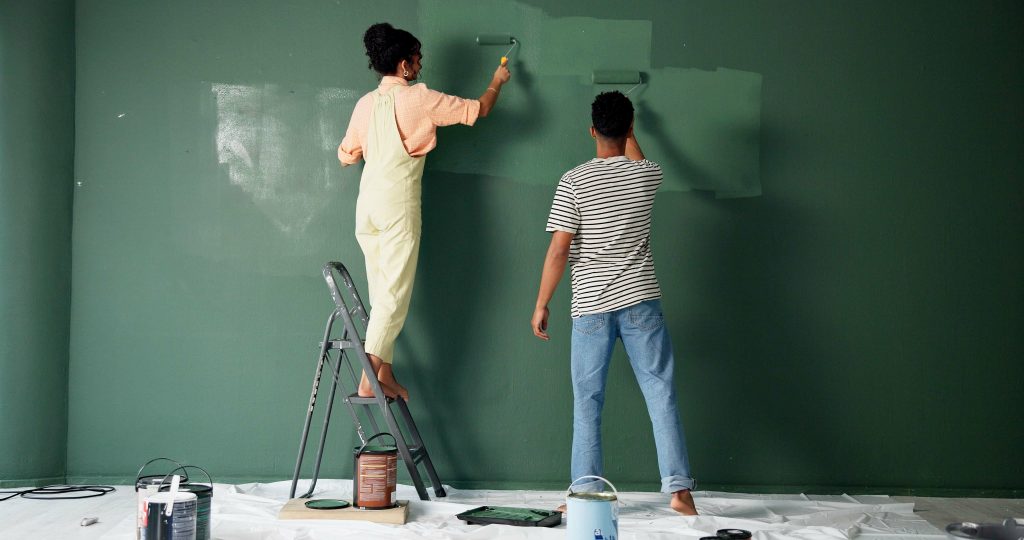 A couple painting a wall green, with the woman standing on a step ladder.