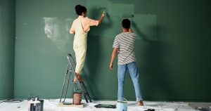 A couple painting a wall green, with the woman standing on a step ladder.