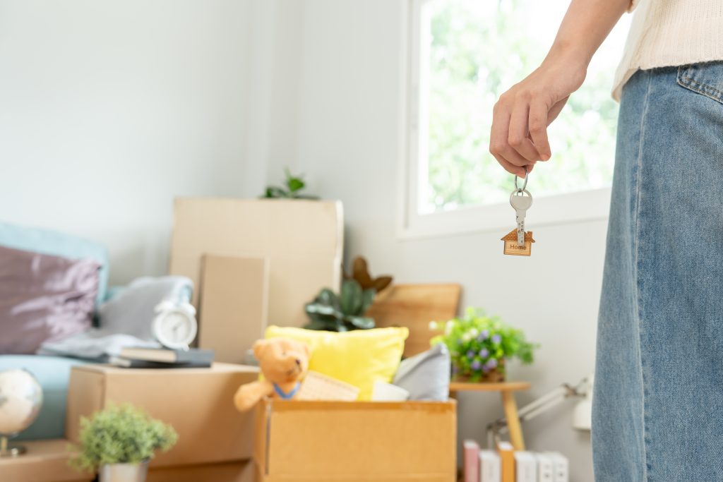 A person stands near full moving boxes, holding an apartment key in their hand.