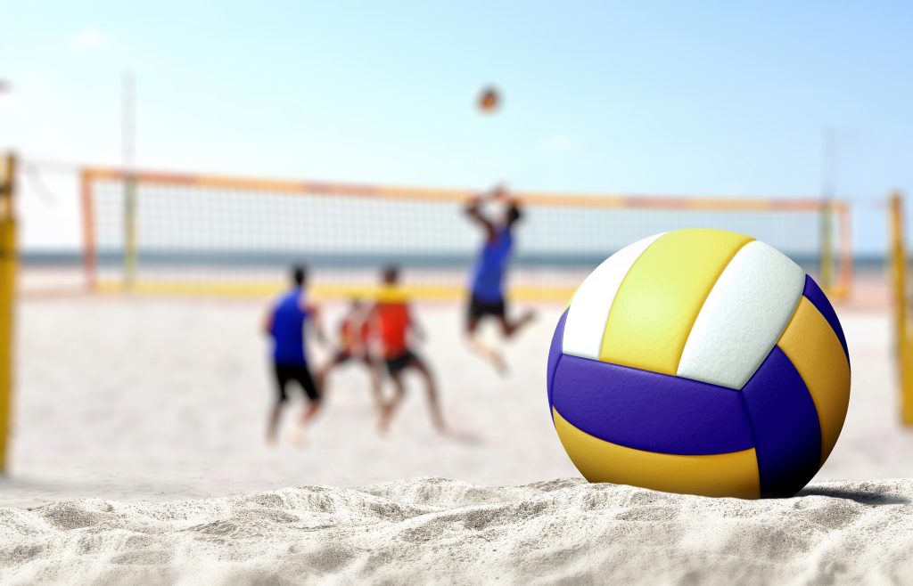 A volleyball in the sand with people playing beach volleyball in the background.