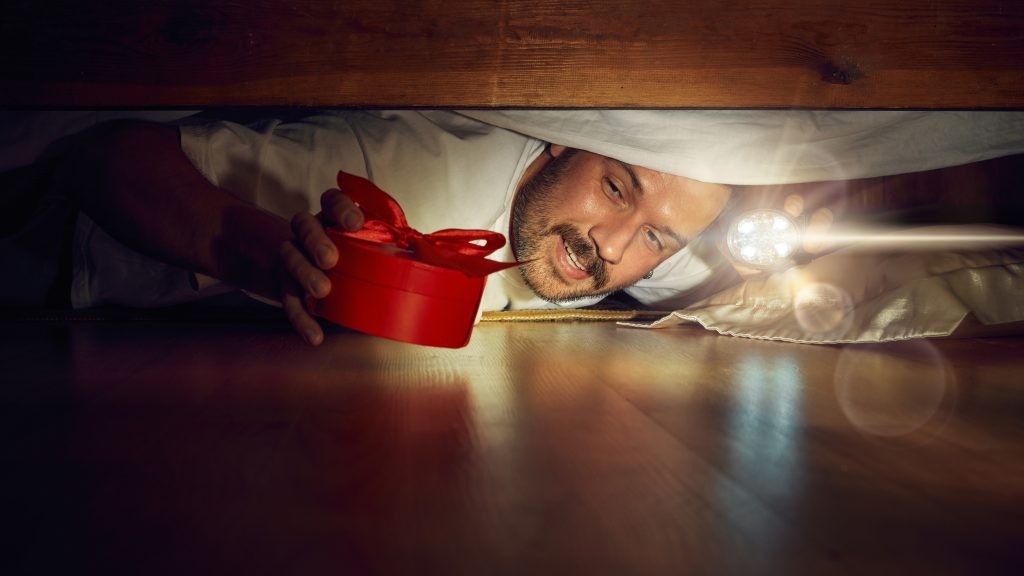 Man hiding christmas present under bed.
