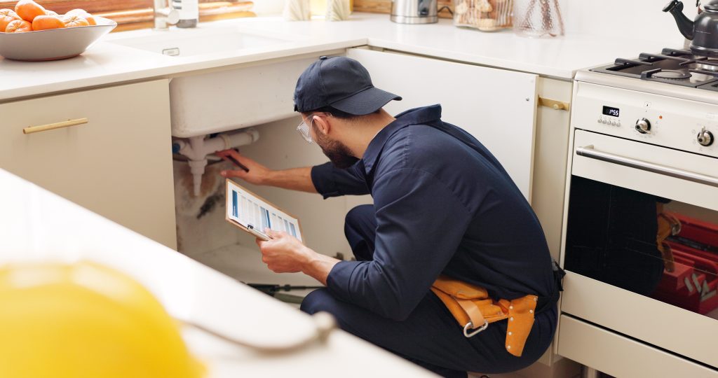 A plumber inspecting the pipes under a kitchen sink.