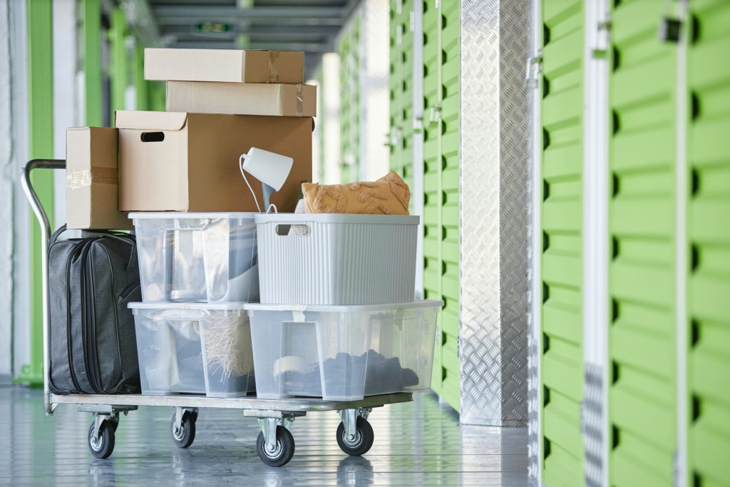 A dolly with totes and boxes parked outside of a closed self storage unit.
