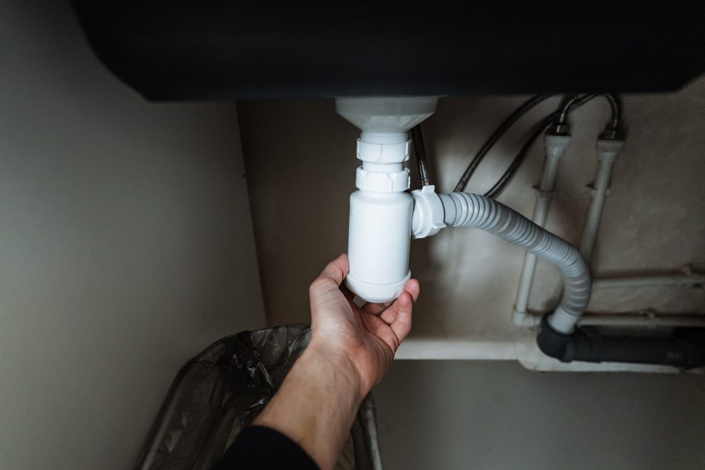 a hand reaching out to check a pipe beneath a sink.