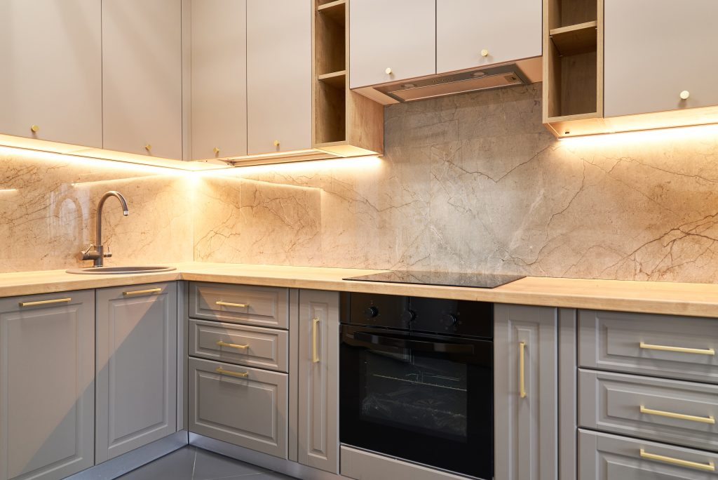 A kitchen space with a marble backsplash, gray cabinets, and gold hardware.