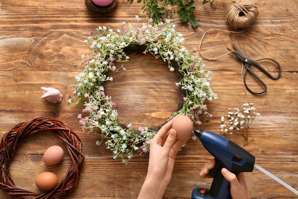Hands building a DIY spring wreath with a glue gun.