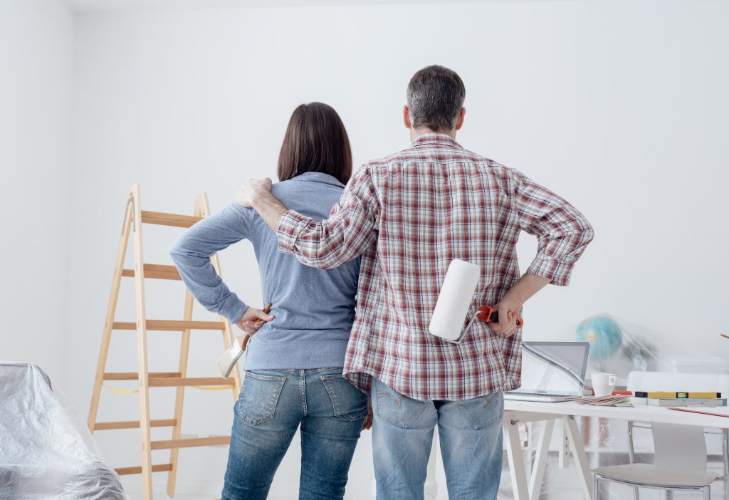 A couple looking proudly at a freshly painted wall surrounded by home improvement tools.