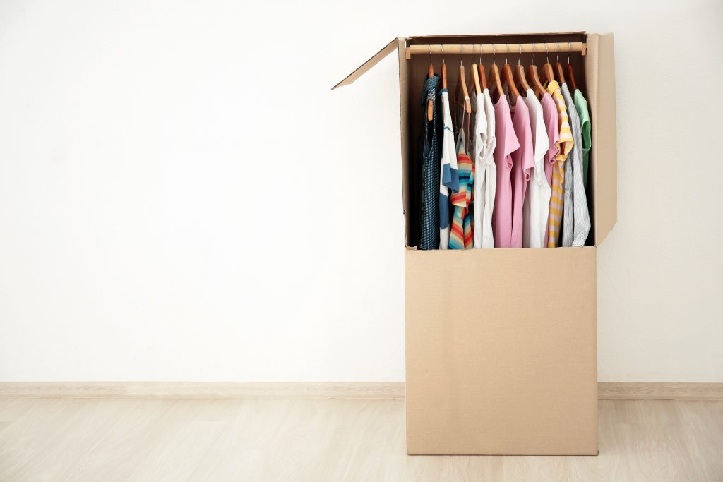 A wardrobe box with shirts hung up in it.
