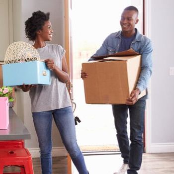 A smiling couple moving cardboard boxes into a new home.